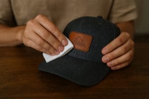 person cleaning leather patch on hat